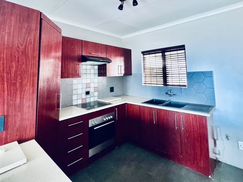 A functional kitchen featuring dark wood-finish cabinetry, integrated oven and hob, tiled splashbacks, and a double sink with a window view.