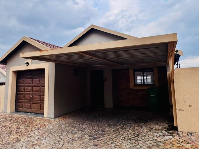 Front exterior view of a townhouse featuring a paved driveway, a single garage, and a covered carport with perimeter walling and electric fencing.