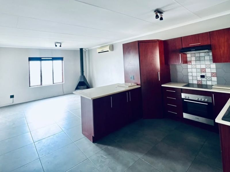 Spacious open-plan living area featuring a modern kitchen with built-in appliances, tiled flooring, a fireplace, and a wall-mounted air conditioning unit.
