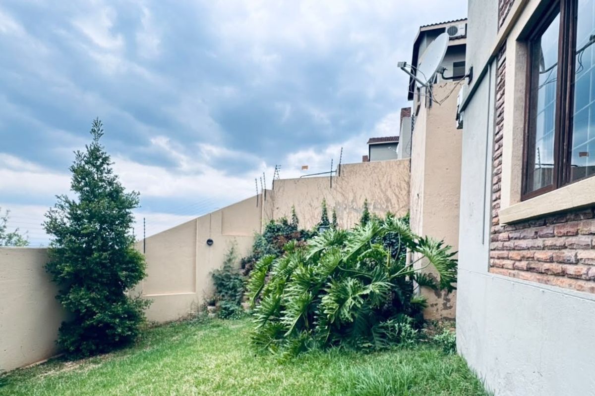 A view of the rear exterior area featuring a lawn, boundary wall with electric fencing, and brick facade detailing.