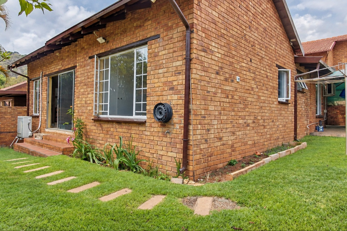 Rear view of a face brick townhouse featuring a small garden, paved stepping stones, sliding door access, and a functional rotary clothesline.