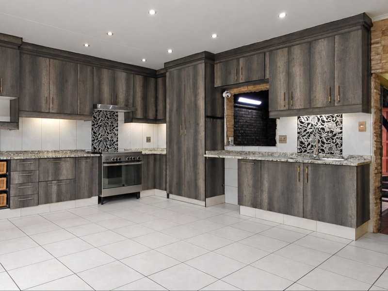 Modern kitchen featuring dark wood cabinetry, granite countertops, stainless steel stove, and tiled flooring with a stone feature wall accent.