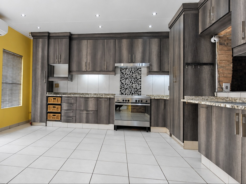 Modern kitchen featuring dark wood cabinetry, granite countertops, stainless steel appliances, and tiled flooring, with direct access to an outdoor area.