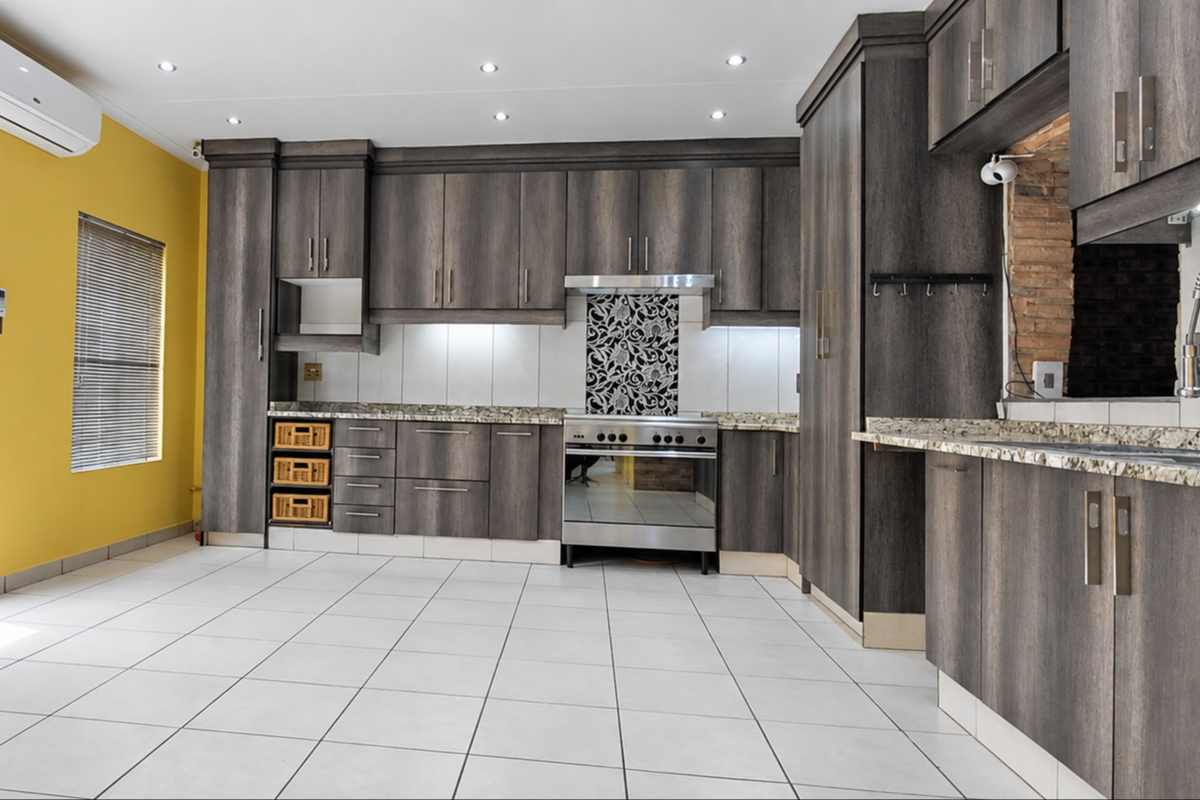 Modern kitchen featuring dark wood cabinetry, granite countertops, stainless steel appliances, and tiled flooring, with direct access to an outdoor area.