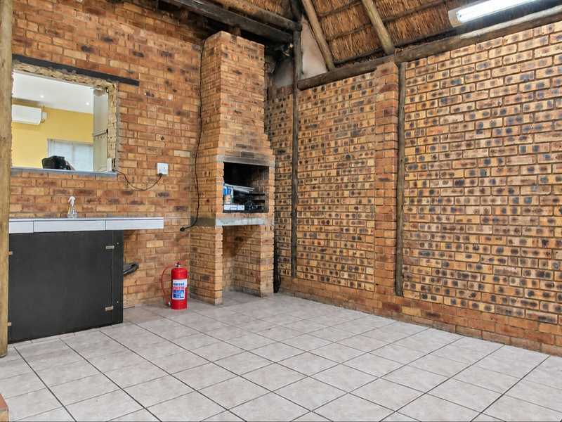 Covered outdoor patio featuring a built-in brick braai, tiled flooring, exposed brick walls, and a traditional thatched roof structure.