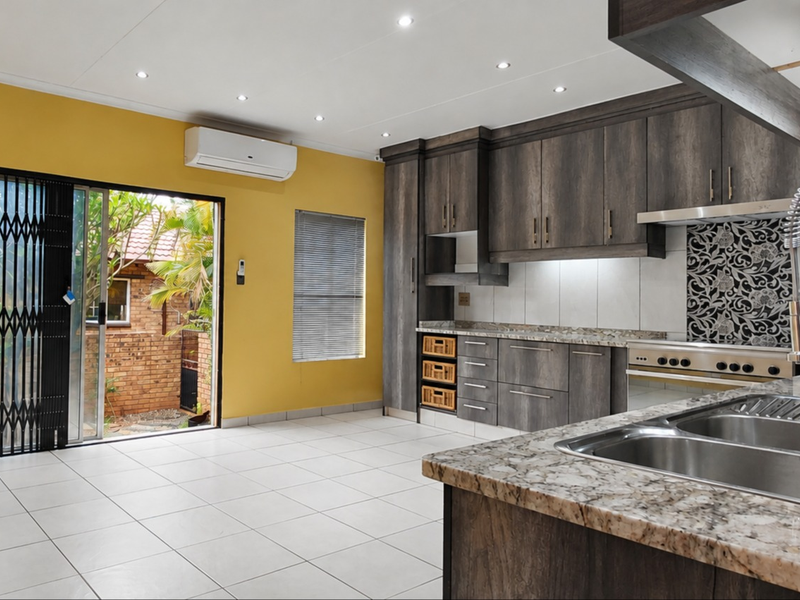 Spacious open-plan kitchen and living area featuring dark wood cabinetry, granite countertops, tiled floors, and direct access to the outdoor area via sliding doors.