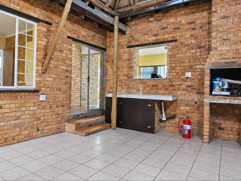 Covered outdoor patio featuring exposed brick walls, a built-in braai, tiled flooring, and direct access to the interior through a sliding glass door.