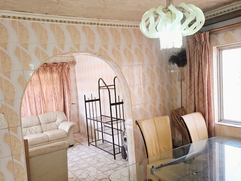 Open plan living and dining area featuring arched architectural detailing, tiled wall finishes, and decorative ceiling tiles in a dated aesthetic.