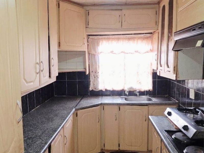 A functional kitchen featuring built-in cabinetry, dark tiled backsplash, laminate countertops, and a gas stove with an extractor fan.
