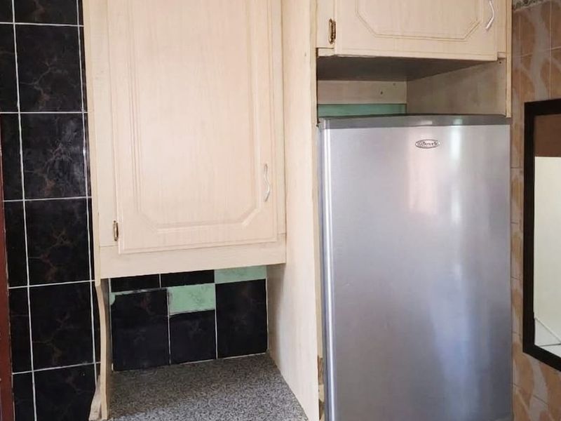 A compact kitchen area featuring built-in cabinetry, granite countertops, and a tiled backsplash, currently showing signs of wear and dated finishes.