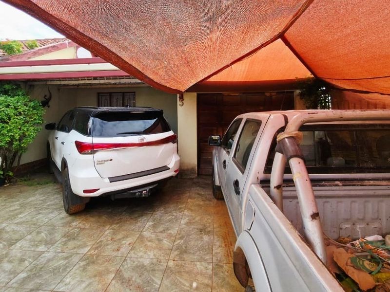 A covered parking area featuring tiled flooring and a shade cloth canopy structure.