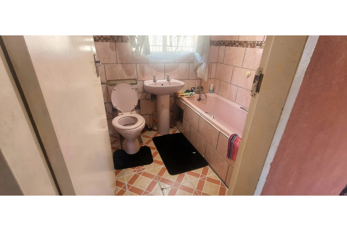 A compact bathroom featuring a pedestal basin, toilet, and bathtub with dated wall and floor tiling.
