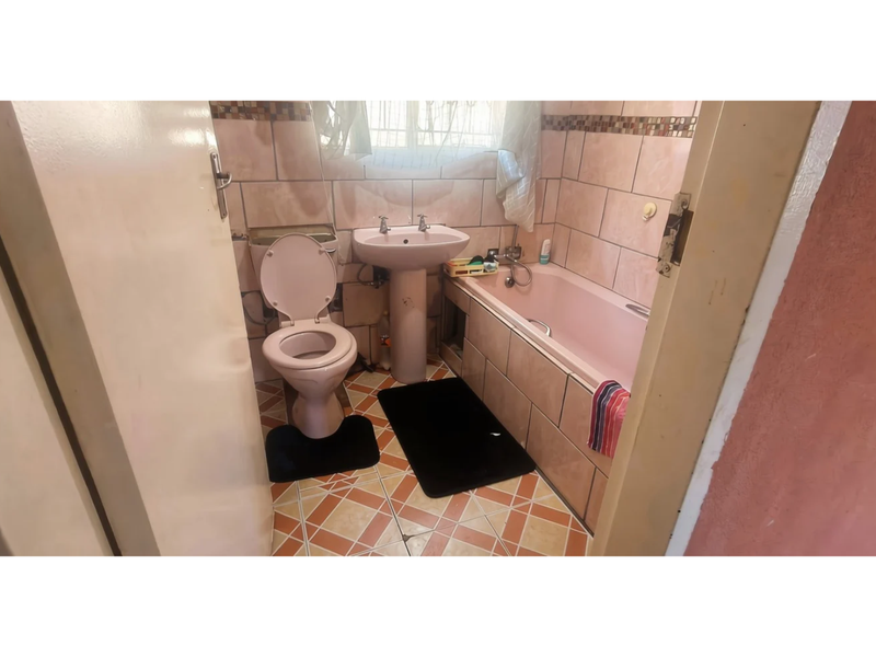 A compact bathroom featuring a pedestal basin, toilet, and bathtub with dated wall and floor tiling.