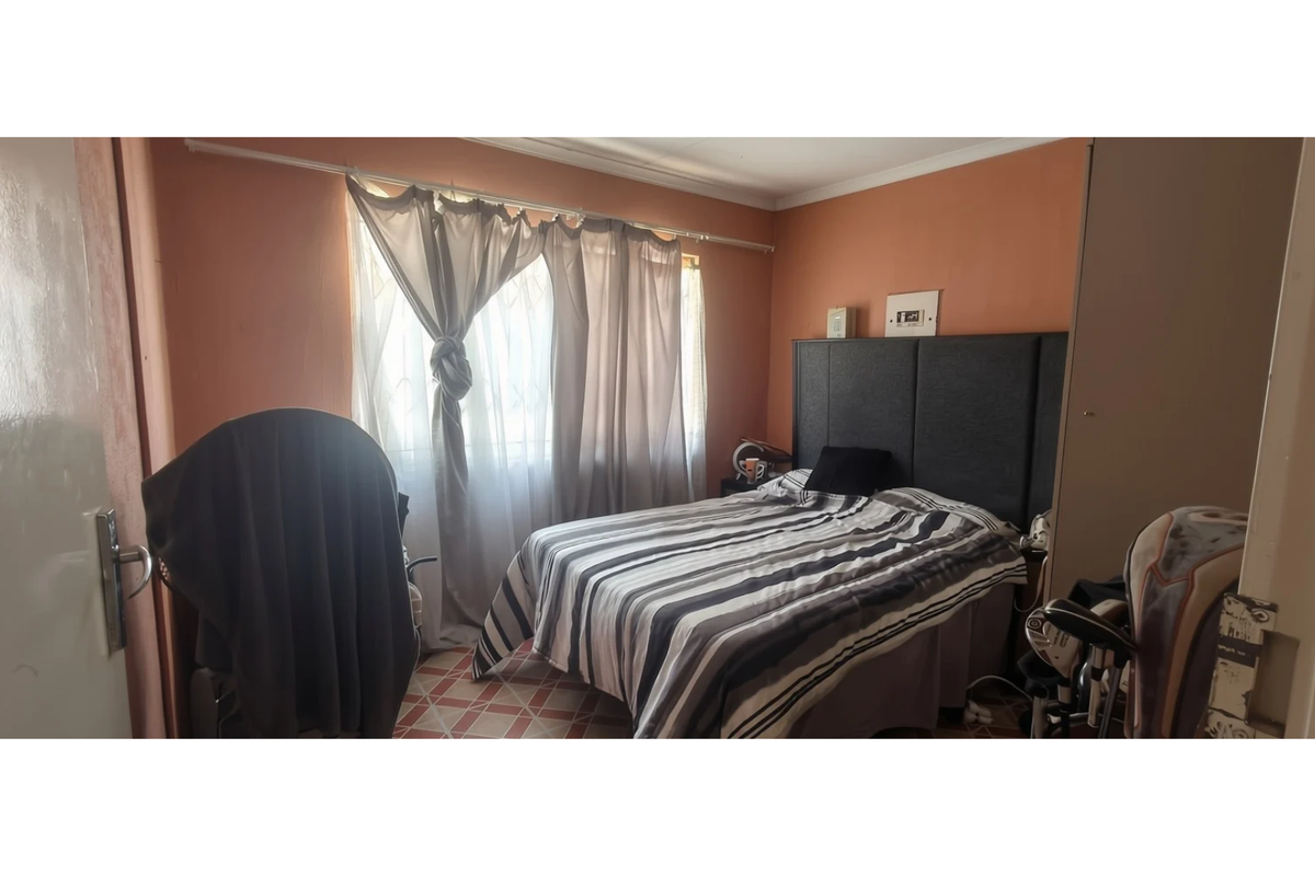 A bedroom featuring tiled flooring and a window with curtain fixtures, requiring cosmetic updates to the wall finishes.