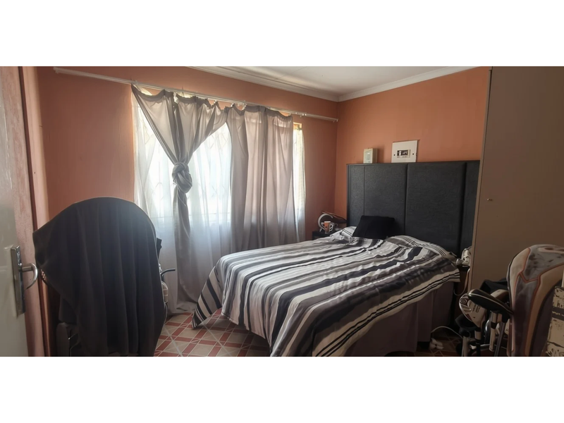 A bedroom featuring tiled flooring and a window with curtain fixtures, requiring cosmetic updates to the wall finishes.