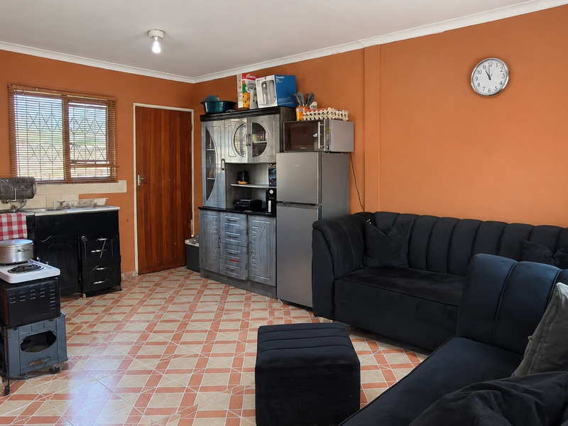 Open plan living area featuring tiled flooring, a compact kitchen corner with sink, and direct access to an exterior door.