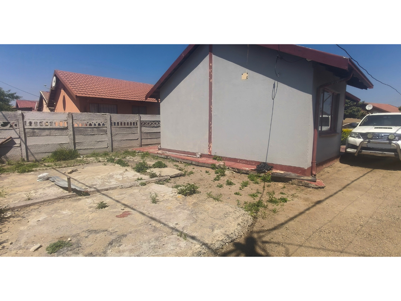 Rear exterior view of the property featuring a concrete slab area, precast boundary wall, and visible wear to the building's exterior paint and finishes.