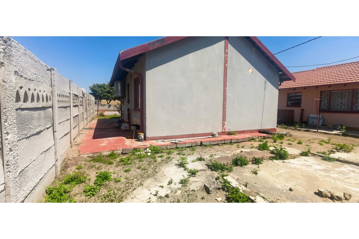 Rear view of the property featuring a precast concrete boundary wall, painted exterior walls, and a concrete apron area requiring landscaping and maintenance.