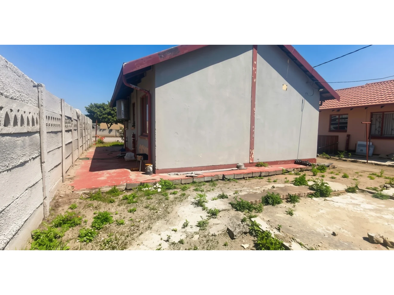 Rear view of the property featuring a precast concrete boundary wall, painted exterior walls, and a concrete apron area requiring landscaping and maintenance.