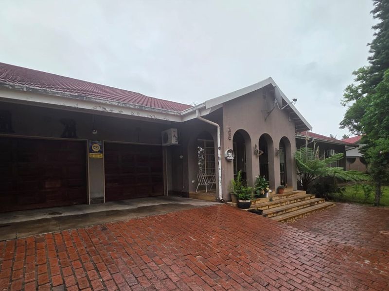 Front elevation of a house featuring a double garage, brick paved driveway, and an arched entrance porch with a tiled roof.