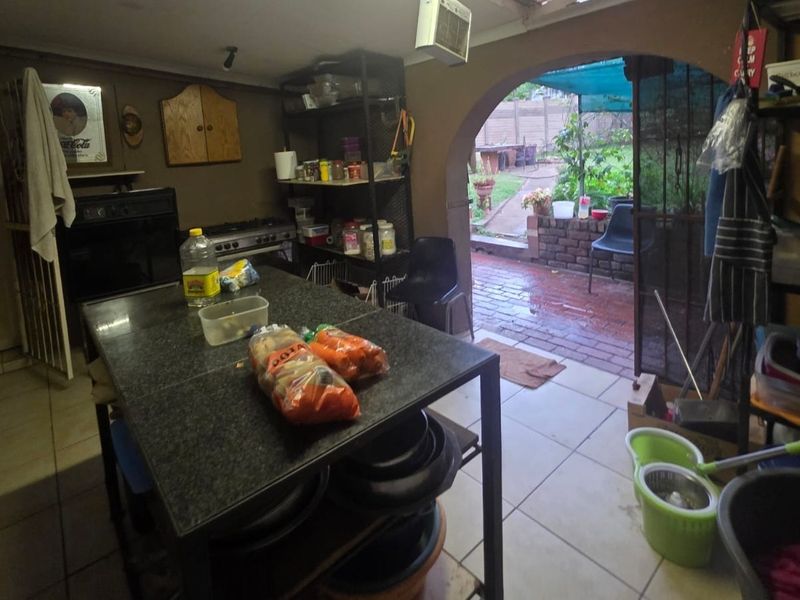 A functional scullery area featuring a built-in oven, gas hob, and tiled flooring, with direct access to the rear patio through an arched doorway.