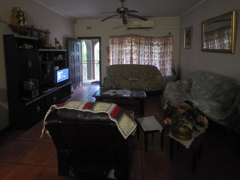 A living room featuring tiled flooring, a ceiling fan, and a wall-mounted air conditioning unit, providing a functional and comfortable living space.