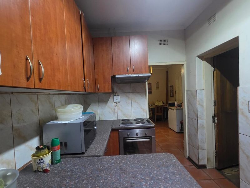 A functional kitchen featuring wood-look cabinetry, laminate countertops, built-in oven with hob, and tiled splashbacks, leading into an adjacent dining area.