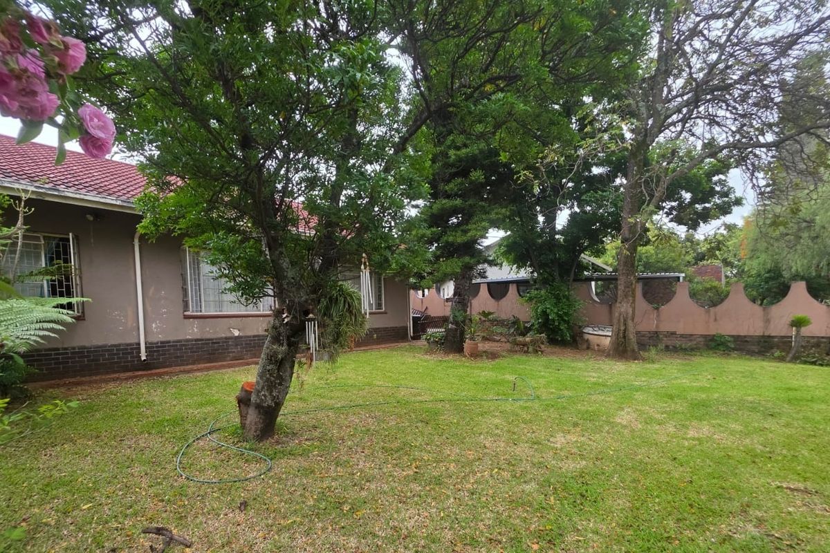 A spacious rear garden featuring a lawn, mature trees, and a boundary wall, providing a private outdoor space for the property.