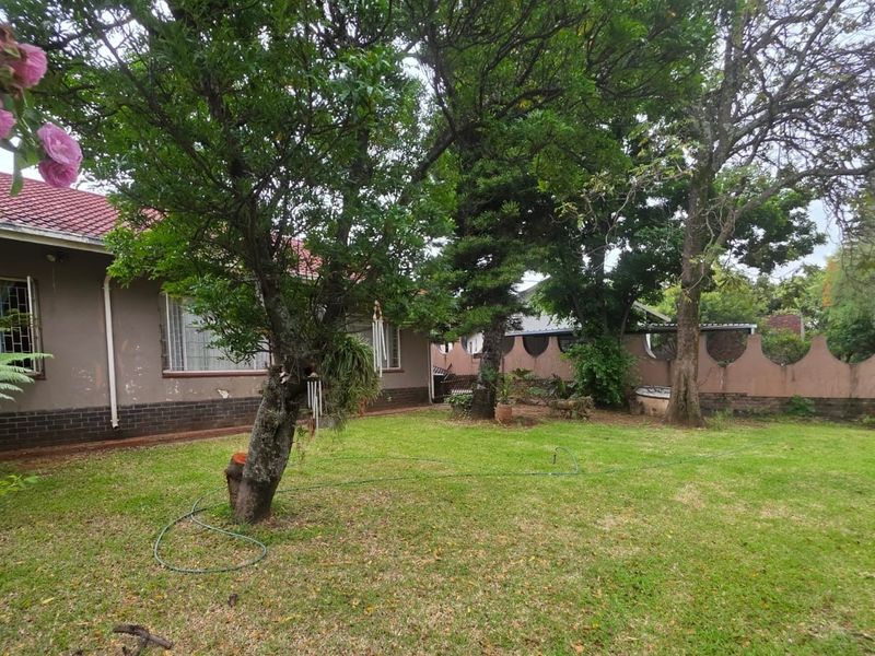 A spacious rear garden featuring a lawn, mature trees, and a boundary wall, providing a private outdoor space for the property.