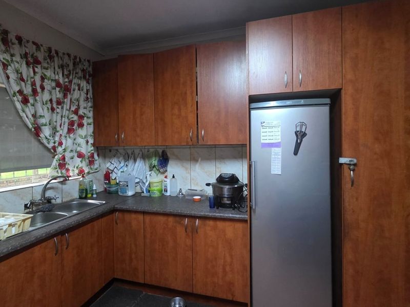A functional kitchen featuring wood-look laminate cabinetry, durable countertops, and a double bowl stainless steel sink with a tiled backsplash.