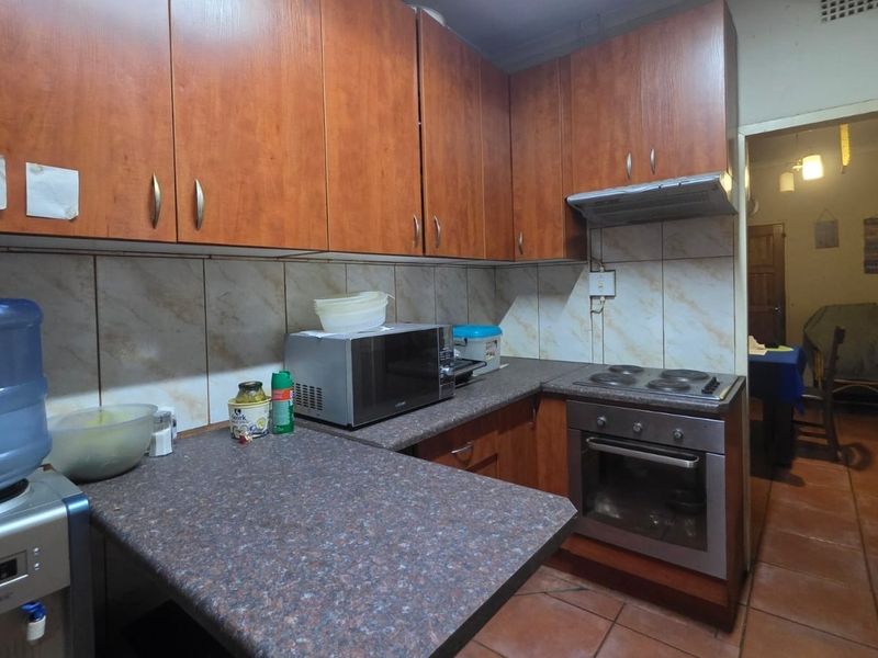A functional kitchen featuring wood-look laminate cabinetry, tiled backsplash, and built-in cooking appliances with tiled flooring.