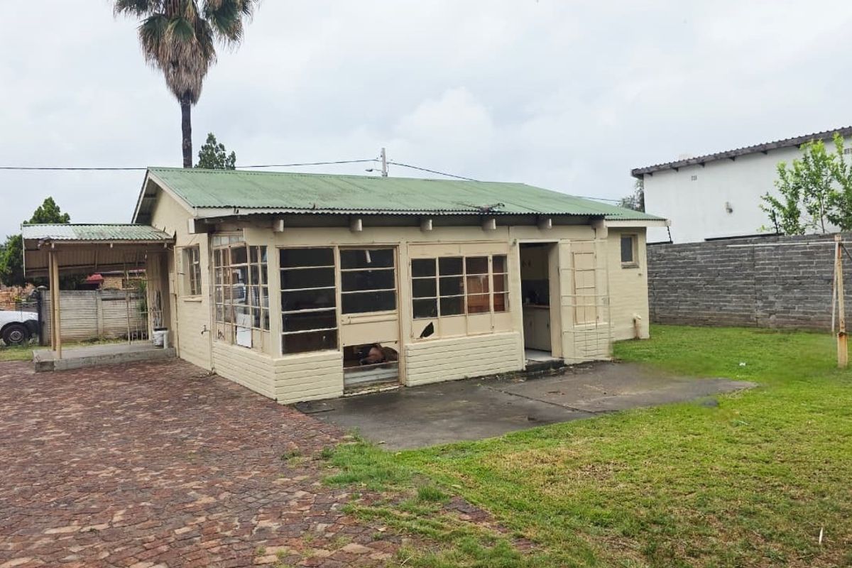 Rear view of a detached dwelling featuring a corrugated metal roof, brick construction, and a paved patio area requiring significant maintenance and repair.