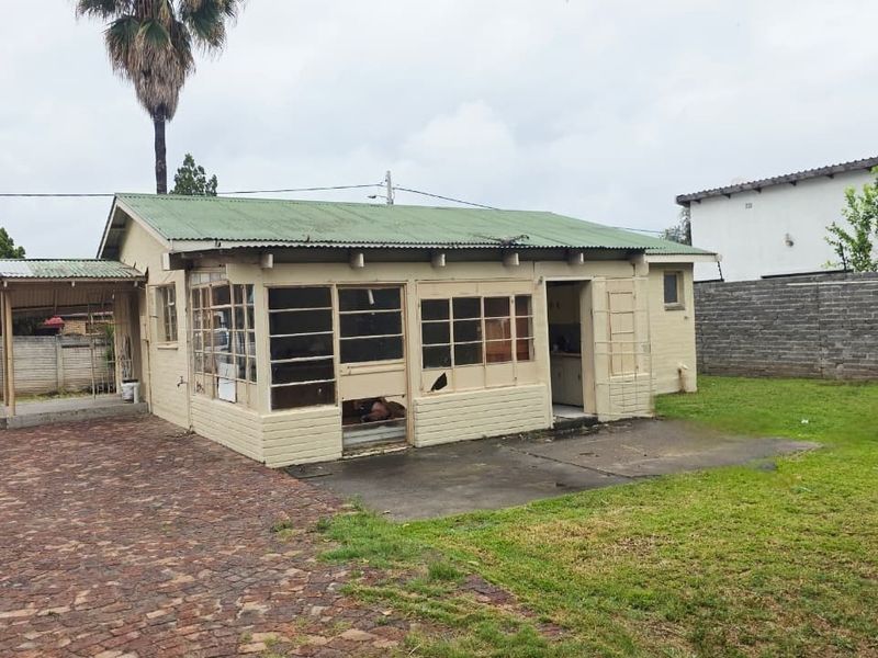 Rear view of a detached dwelling featuring a corrugated metal roof, brick construction, and a paved patio area requiring significant maintenance and repair.