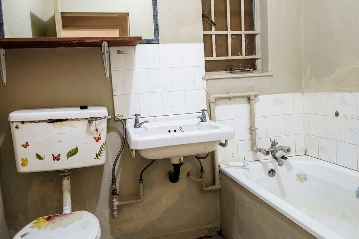 A dated bathroom featuring a wall-mounted basin, bathtub, and toilet, requiring significant renovation and modernization of fixtures and finishes.