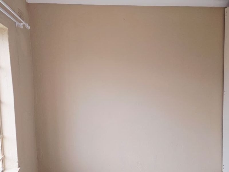 A vacant bedroom featuring a built-in cupboard and a window fitted with security bars.