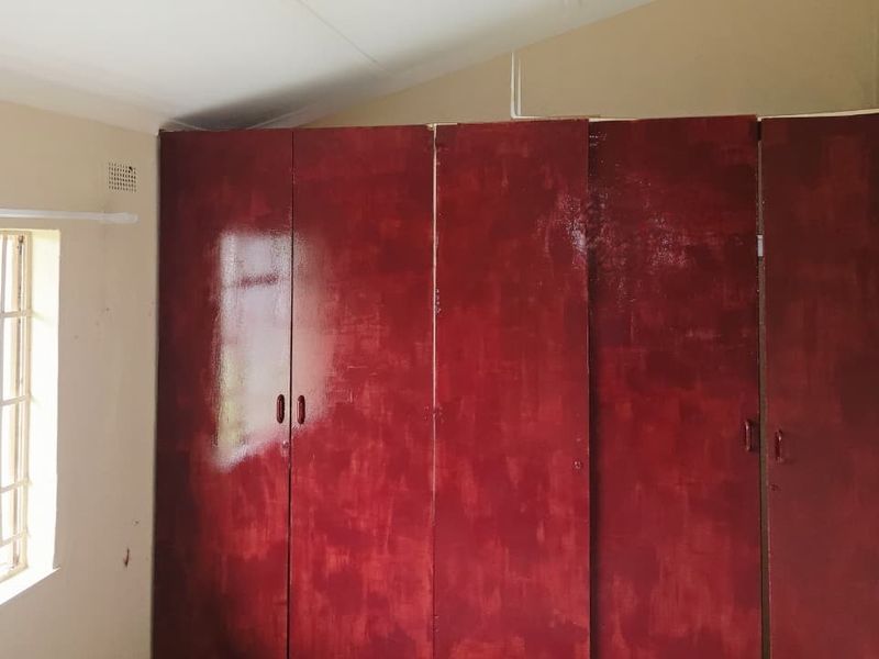 A bedroom featuring built-in cupboards with a red finish and a window fitted with security burglar bars.