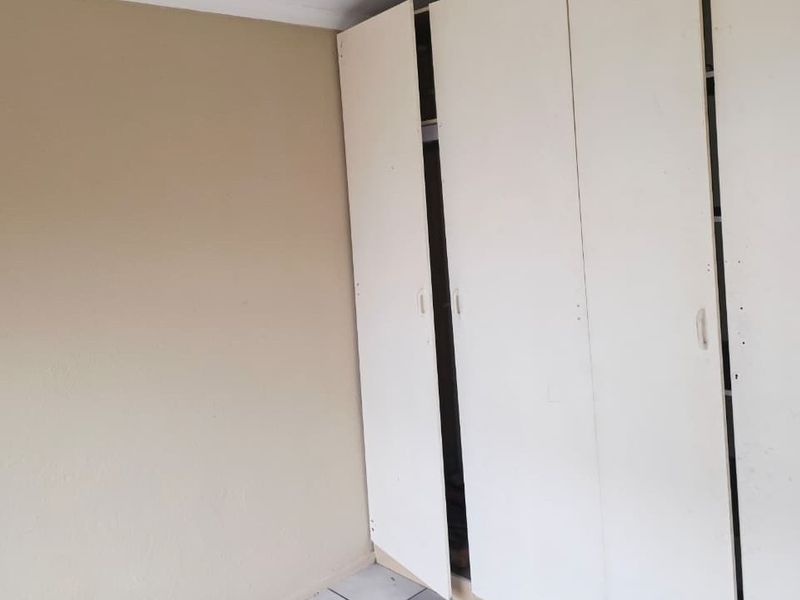 A vacant bedroom featuring built-in cupboards with visible wear and misaligned doors, offering a blank canvas for potential updates.