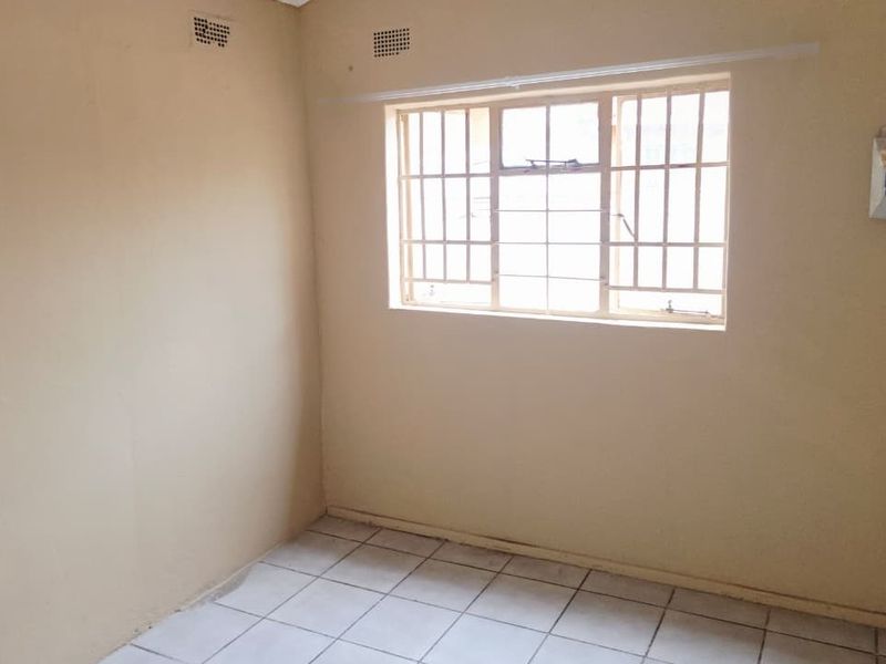 An empty bedroom featuring tiled flooring, a window with security bars, and a wall-mounted electrical distribution board.