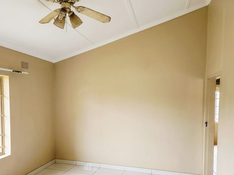 An empty bedroom featuring a vaulted ceiling, tiled flooring, and a ceiling fan, with security bars installed on the window.