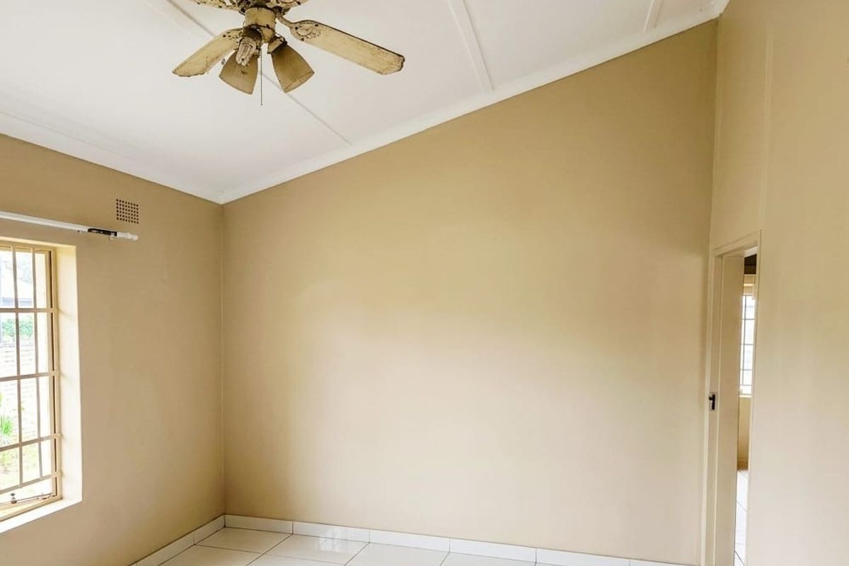 An empty bedroom featuring a vaulted ceiling, tiled flooring, and a ceiling fan, with security bars installed on the window.