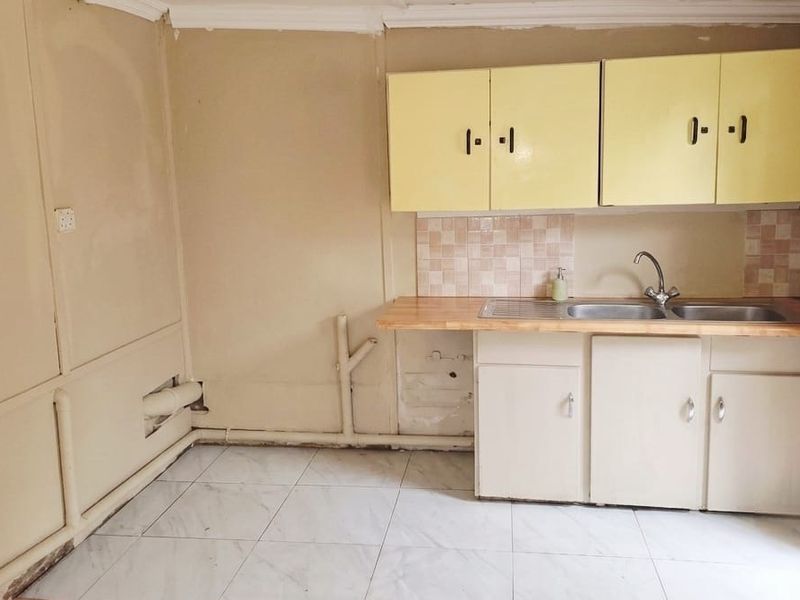 A compact, dated kitchen featuring basic cabinetry, a double bowl sink, and tiled flooring, requiring cosmetic updates and finish improvements.