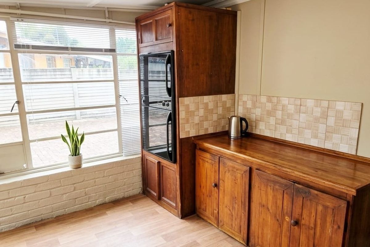 A functional kitchen area featuring wooden cabinetry, a built-in oven, tiled backsplash, and large windows providing natural light.