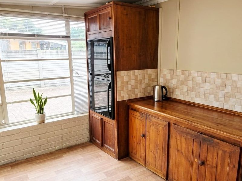 A functional kitchen area featuring wooden cabinetry, a built-in oven, tiled backsplash, and large windows providing natural light.