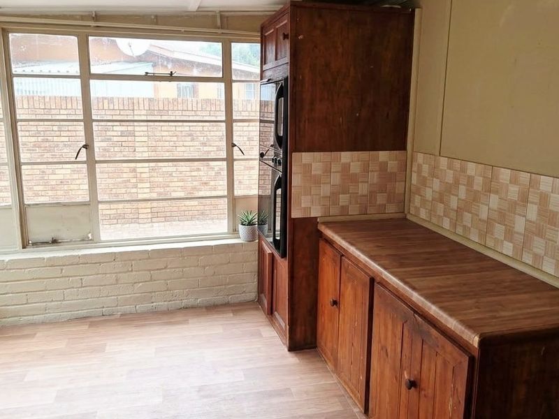 A dated kitchen area featuring built-in wooden cabinetry, a laminate countertop, and a large window providing natural light.