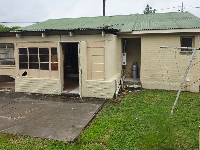 Rear view of the property featuring a concrete patio, brick exterior walls, and a corrugated metal roof with visible maintenance requirements.
