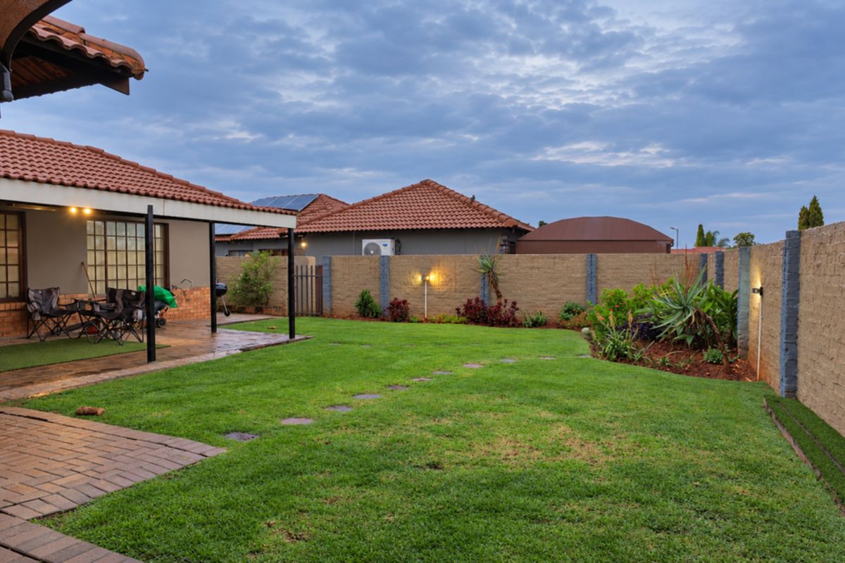 A well-maintained rear garden featuring a covered patio, paved pathways, and secure brick boundary walls with integrated outdoor lighting.