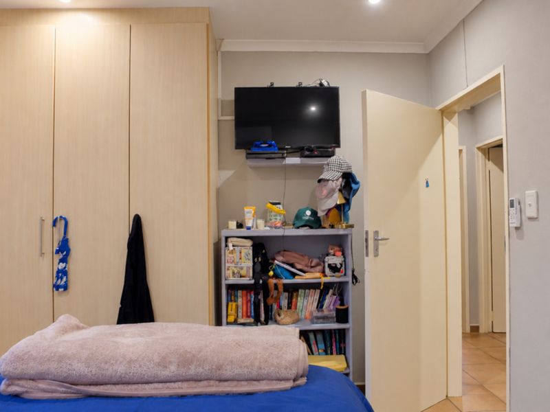 A functional bedroom featuring built-in wardrobes, recessed downlighting, and tiled flooring, providing a practical living space with neutral finishes.