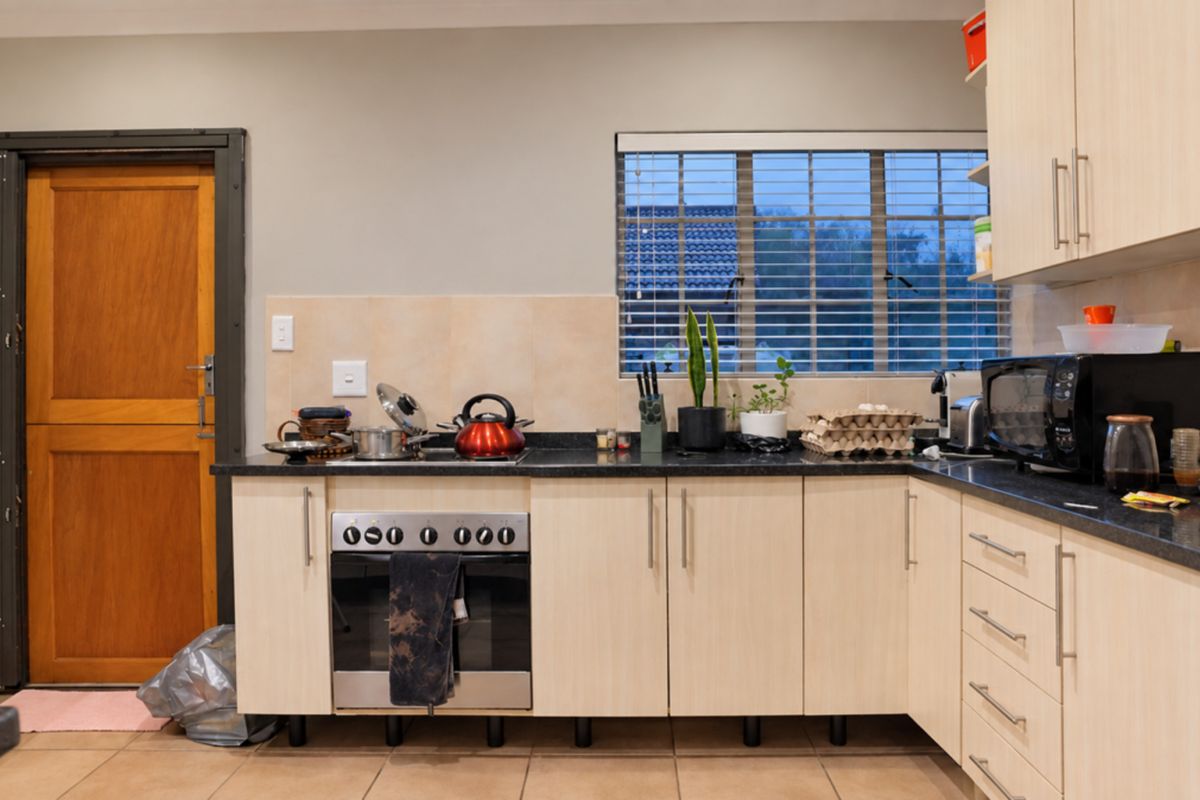 A functional kitchen featuring light wood-finish cabinetry, granite countertops, a built-in oven, and tiled flooring with direct access to an exterior door.
