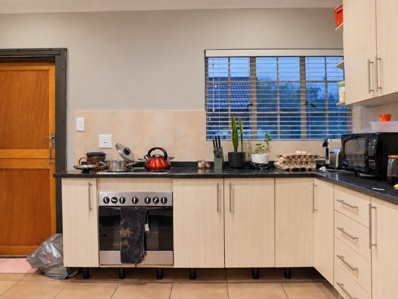 A functional kitchen featuring light wood-finish cabinetry, granite countertops, a built-in oven, and tiled flooring with direct access to an exterior door.