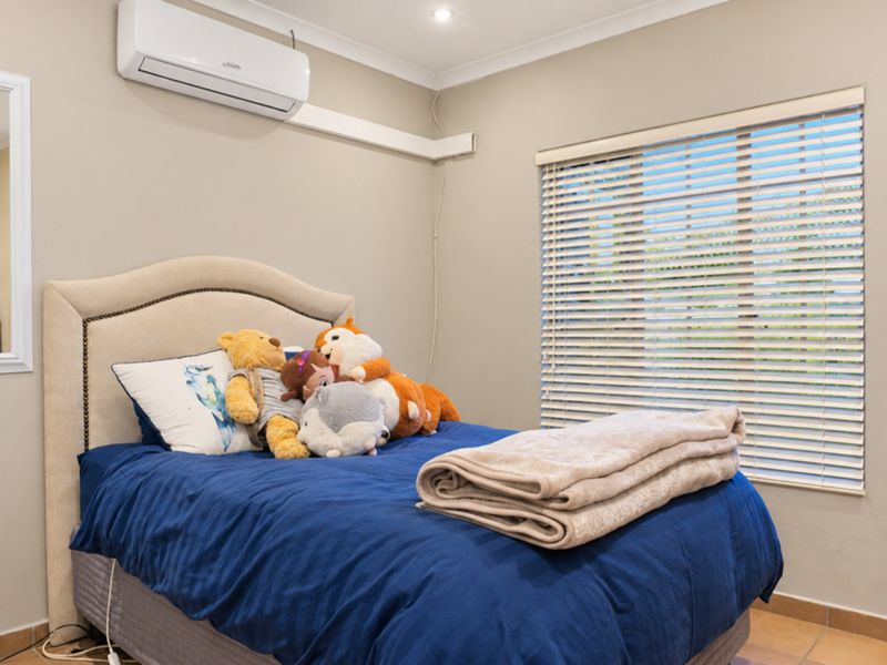 A well-maintained bedroom featuring tiled flooring, a wall-mounted split-system air conditioner, and venetian blinds for light control.